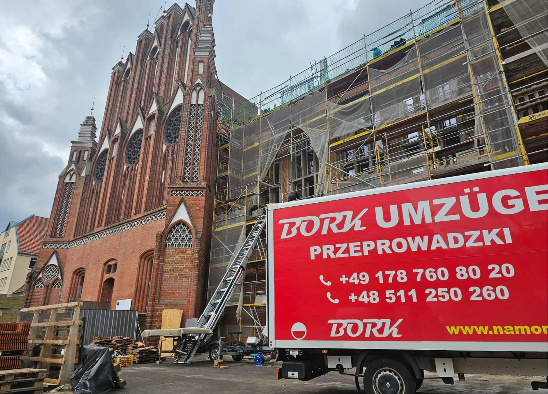 Bork Umzüge Transporter vor einer neogotischen Backsteinkirche mit Baugerüst
