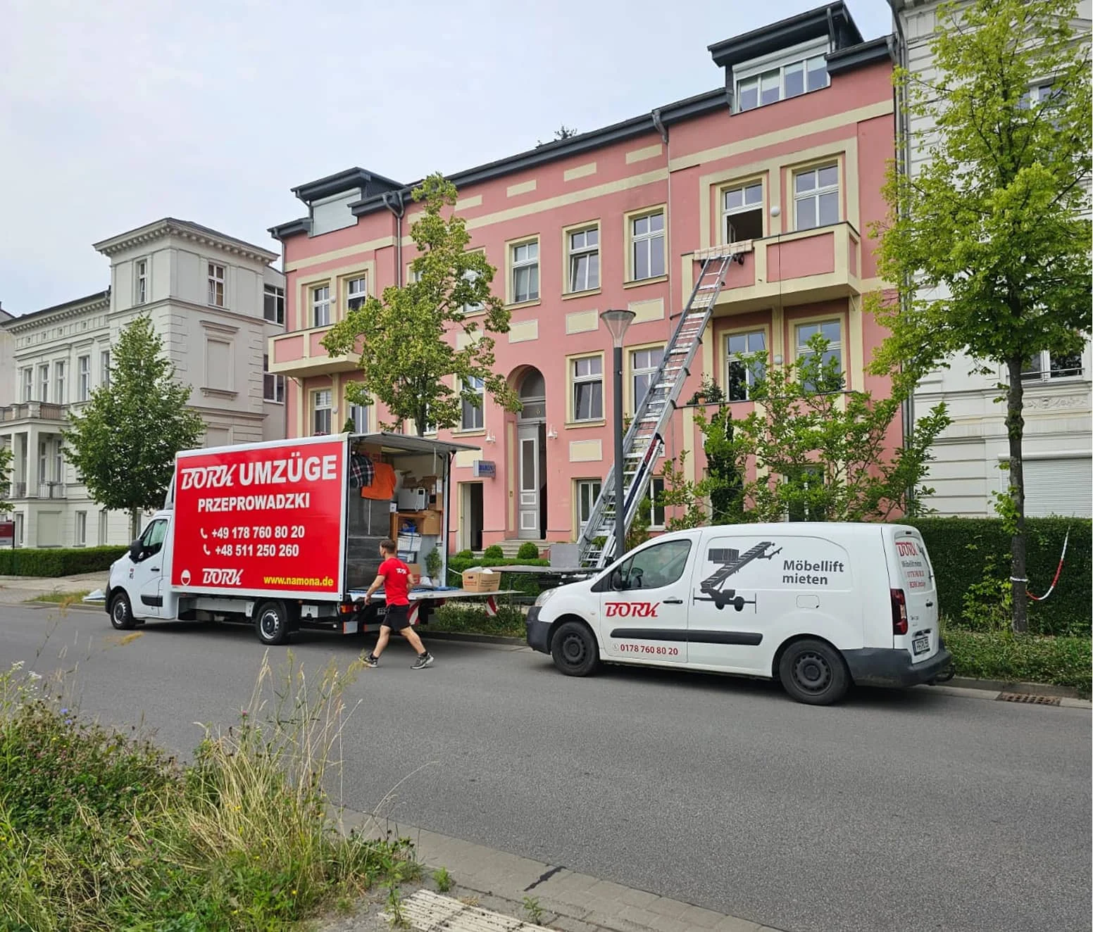 Bork Umzüge LKW und Möbellift-Fahrzeug vor einem rosa Altbau, Mitarbeiter trägt Karton