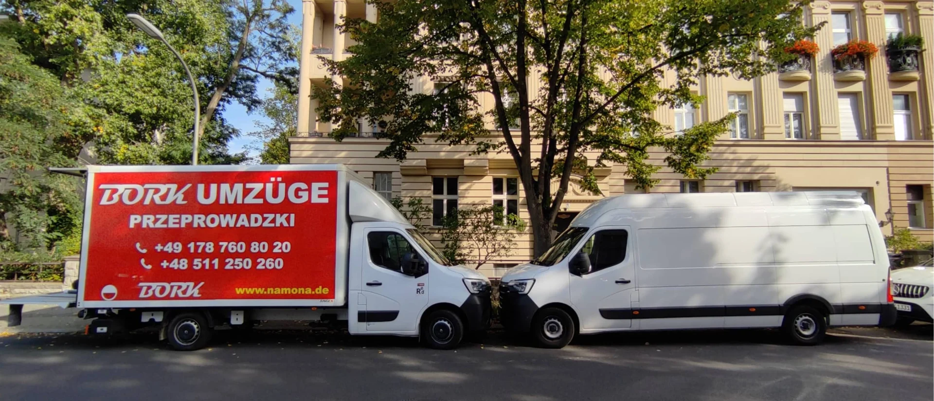 Bork Umzüge LKW mit rotem Werbepanel neben weißem Kastenwagen, parkend vor einem Altbau